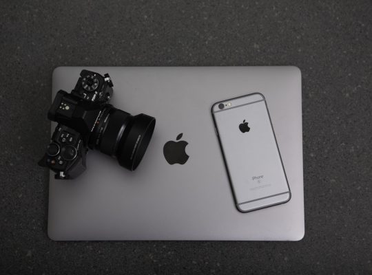 Un ordinateur de marque apple, sur lequel sont disposés un appareil photo et un téléphone portable