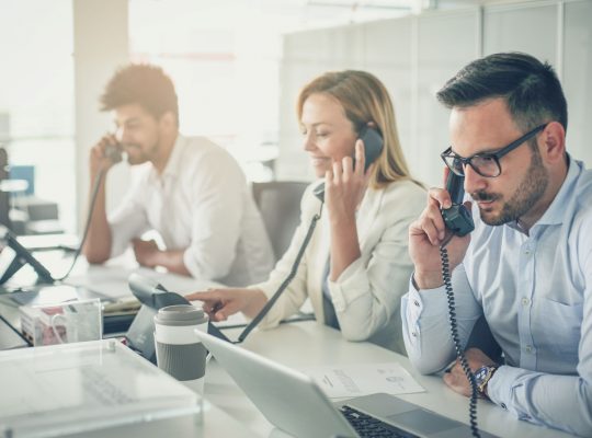 Deux hommes et une femme dans un open space aux téléphones