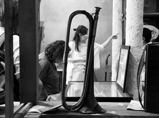 Visite du musée : au premier plan une trompette, au deuxième plan une femme regarde une vitrine, en arrière plan une femme pointe du doigt un élément hors cadre.