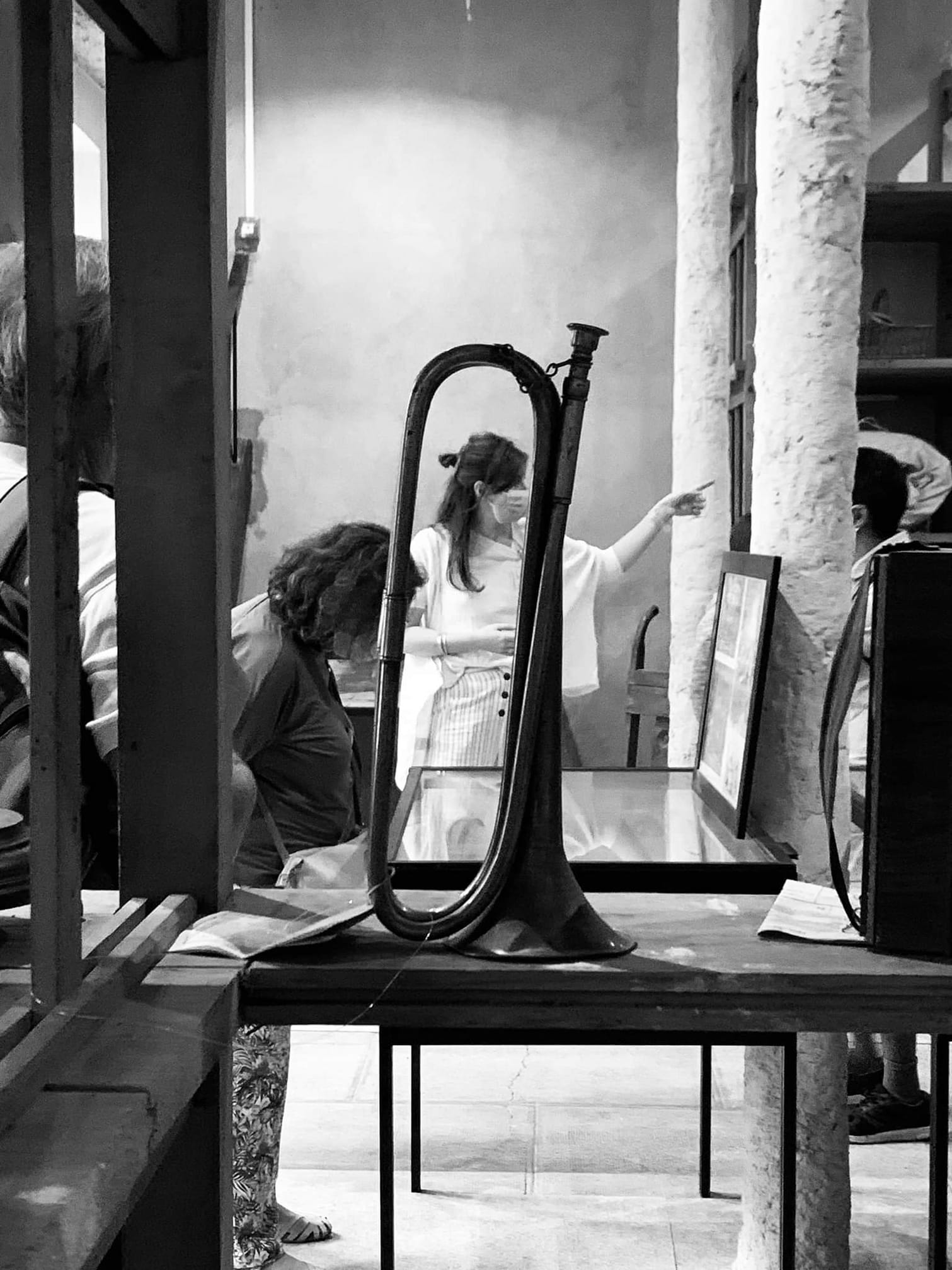Visite du musée : au premier plan une trompette, au deuxième plan une femme regarde une vitrine, en arrière plan une femme pointe du doigt un élément hors cadre.
