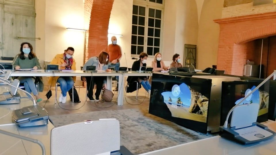 Une salle de réunion avec en arrière plan des personnes assises portant des masques chirurgicaux
