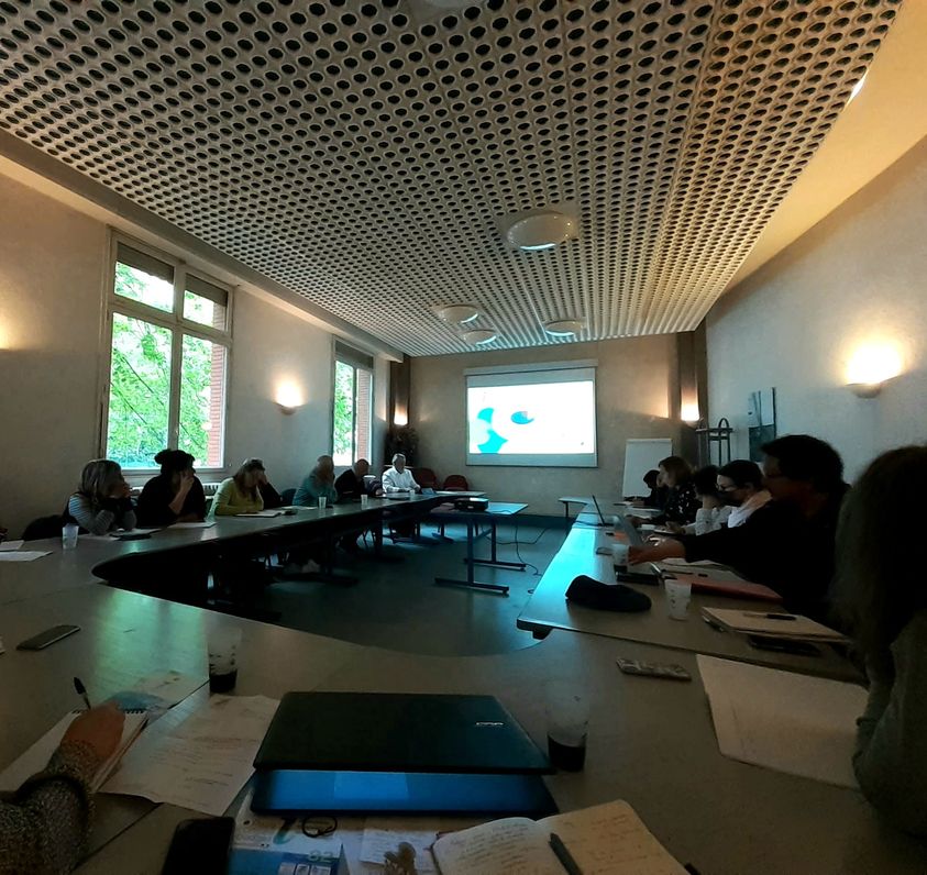 La photographie d'une salle de réunion en forme de U avec une écran de projection allumé à l'arrière plan.