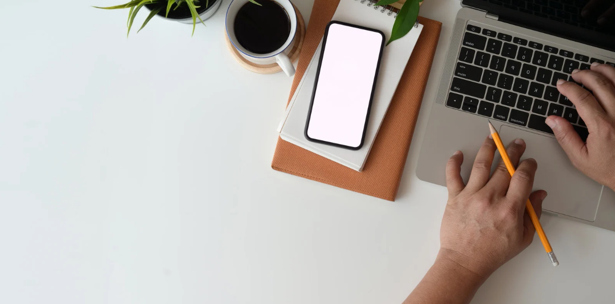 Vue du ciel, un bureau sur lequel est posé une plante, une tasse de café un carnet, un téléphone portable et un ordinateur