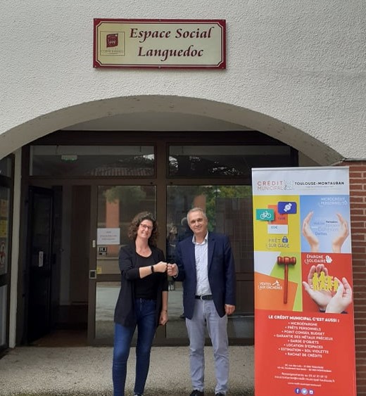 Deux personnes se tenant devant l'entrée du CCAS de Cornebarrieu et proche d'un kakémono du Crédit Municipal de Toulouse se tapant le point amicalement.